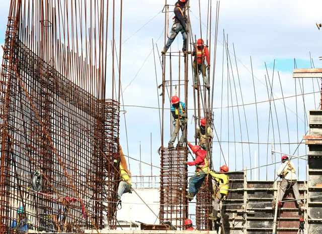 Construction workers on steel rebar scaffolding at a building site under a bright sky