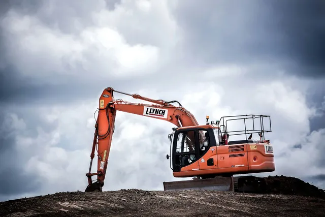 Orange excavator on a dirt mound under a cloudy sky