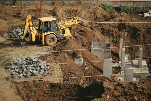 Yellow backhoe excavator working at a construction site with dirt piles and concrete foundations