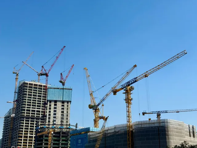 Construction site with tall cranes and partially built high-rise buildings under a clear blue sky
