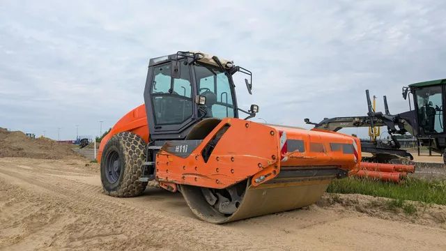 Orange road roller parked on a dirt lot beside another heavy construction machine