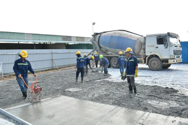 Construction workers paving a road beside a cement mixer truck, wearing hard hats and safety gear.