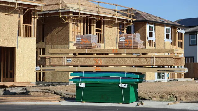 Partially built house with wooden framing and a green dumpster in front