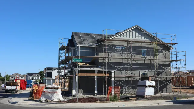 House under construction with scaffolding, exposed framing, and building materials on a clear day