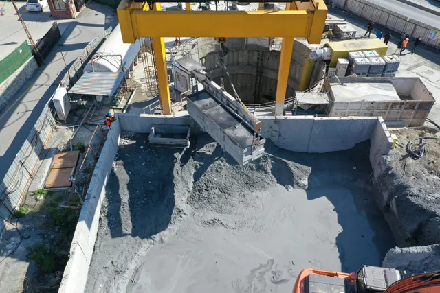 Concrete excavation site with yellow crane pouring wet concrete into a large pit