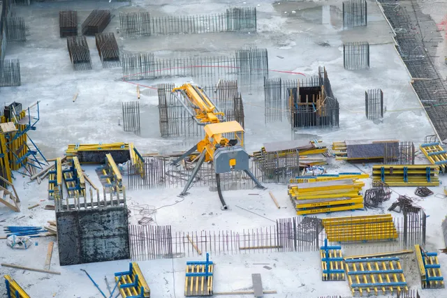 Construction site with a yellow excavator and concrete foundations in a snowy, unfinished building area