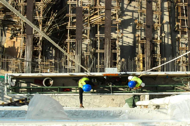 Two workers in yellow vests inspect a large pipe at a construction site.