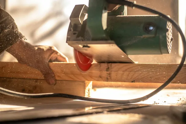Hands guiding a circular saw cutting wood, with sawdust flying in a workshop