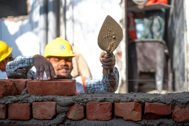 Construction worker in yellow hard hat laying bricks on a wall with a trowel