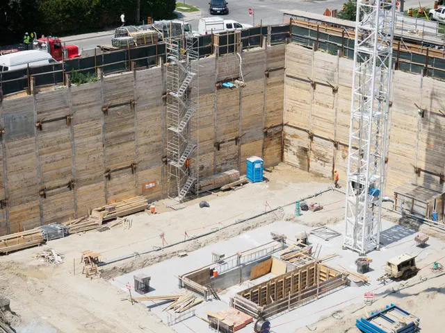 Deep construction pit with concrete walls, scaffolding, and equipment at an urban site