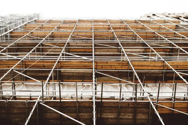 Scaffolding wrapped around a building facade under construction, with wooden planks and metal poles