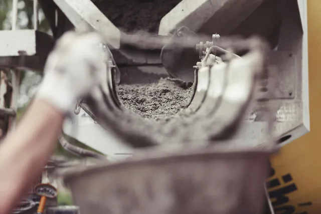 Gloved hands holding a metal part over a bin of gray gravel or concrete debris.