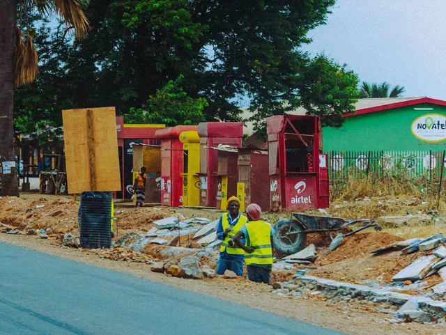 Roadside utility work with workers in yellow vests beside a street and red equipment booths