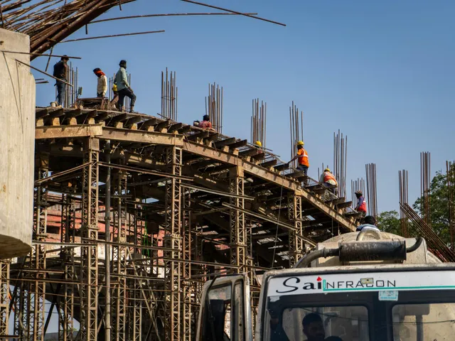 Workers on scaffolding building a curved concrete structure beside a truck under a blue sky