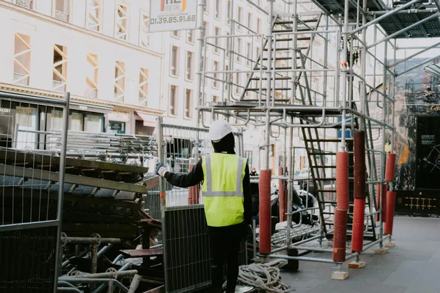 Construction worker in a yellow vest on a scaffold beside a building under renovation