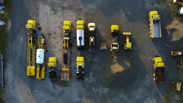 Aerial view of several yellow and white construction vehicles parked on muddy ground.
