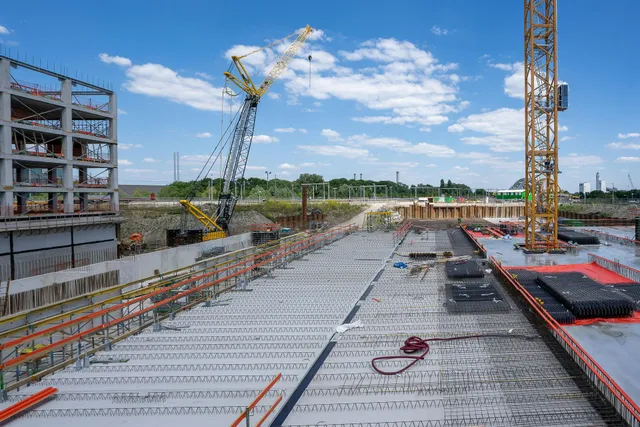 Construction site with concrete foundation, cranes, and a partially built structure under a blue sky