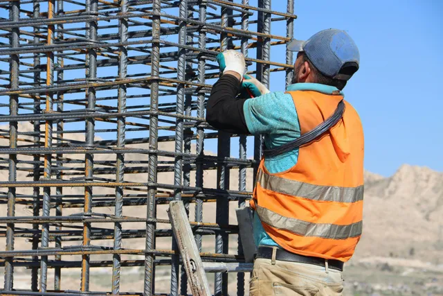Construction worker in orange vest tying rebar on a building frame outdoors