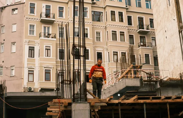 Construction worker in red jacket standing on a scaffold in front of apartment buildings