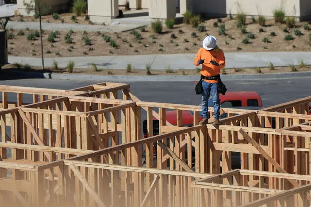 Construction worker in orange vest and hard hat standing on wooden framing at a building site