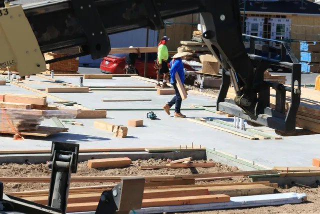 Construction workers guiding a large raised structure over a wooden deck foundation.
