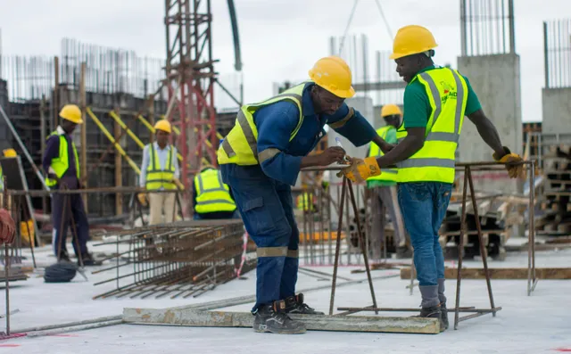 Construction workers in hard hats and safety vests bending rebar at an active building site