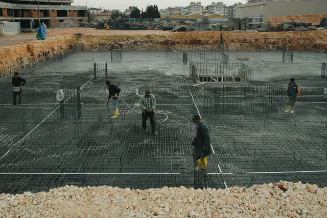 Workers installing rebar in a large concrete foundation pit at a construction site