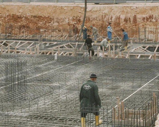 Workers standing over a rebar foundation at a construction site, with an excavated wall in the background