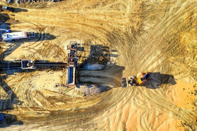 Aerial view of a construction site with heavy machinery and dirt piles in a sandy excavation area