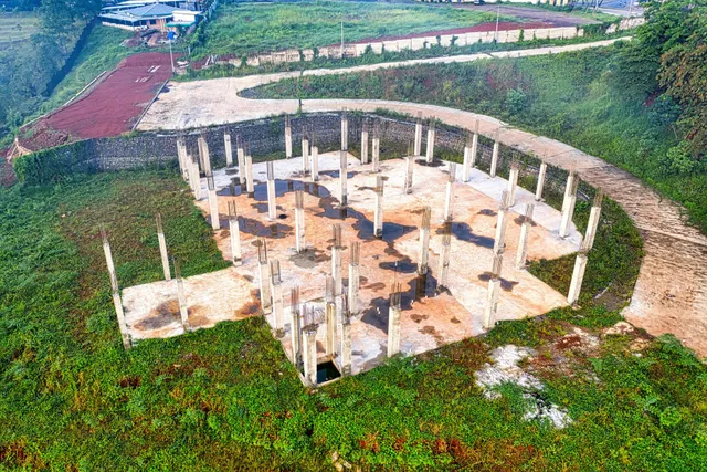 Circular concrete structure under construction in a grassy field, with columns and a central opening