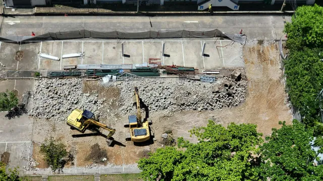 Aerial view of a demolition site with two yellow excavators clearing rubble beside a concrete slab.