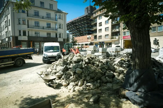 Pile of rubble on a city street near buildings, a white van, and construction barriers in bright daylight