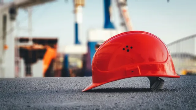 Red hard hat on pavement at a construction site with blurred cranes in the background